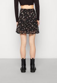 Gonna nera floreale con un design a strati, realizzata in un tessuto leggero. Presenta piccoli fiori colorati, abbinata a stivali neri alla caviglia.