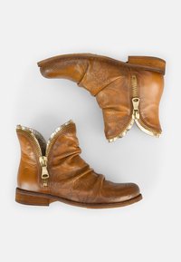 Braune Lederstiefeletten mit einem legeren Design, goldenen Reißverschlussakzenten und dekorativen Perforationen im Obermaterial. Flacher Holzabsatz.