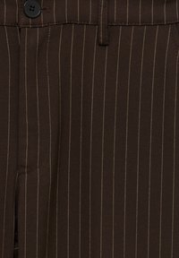 Bruna ränder på byxor med en slät textur, med en svart knapp och subtil sömnad. Klassisk design med skräddarsydd passform.