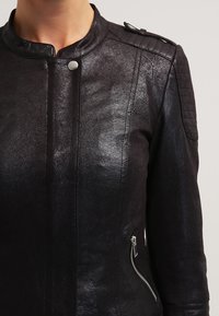 Zbliżenie czarnej skórzanej kurtki z kołnierzem na napy, zasuwanym bocznym kieszeniem i pikowanym wykończeniem na ramionach.
