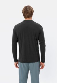 Maglietta nera a maniche lunghe, realizzata in tessuto morbido, presenta un design semplice con scollatura tonda e maniche aderenti.