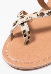 Sandály se syntetickou podrážkou barvy opálené kůže s texturovaným povrchem a páskem s leopardím vzorem z chlupatého materiálu. Design s překříženými pásky.