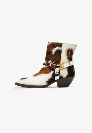 Botte de cowboy mi-mollet avec motif en peau de vache marron et blanc, bride à boucle dorée et talon empilé incliné sur fond blanc.