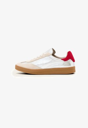 Sneakers with a tan rubber sole, beige suede upper, silver metallic accents, and red heel patch; features flat laces and stitched details.