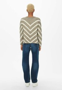 Pull en tricot rayé khaki et blanc avec un col rond, associé à un jean bleu taille haute et des baskets blanches à plateforme.