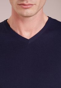 Pull col en V bleu marine en tissu tricoté côtelé. Présente une coupe près du corps avec une texture subtile et des bords sans coutures autour de l'encolure.