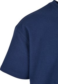 Sötétkék, texturált póló, amely hullámos kötésmintával, rövid ujjal és kerek nyakkivágással rendelkezik. Puha anyag.