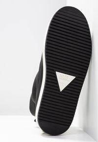 Baskets noires avec une tige en cuir texturé. La semelle en caoutchouc blanc présente un logo triangulaire et un profil cranté pour l'adhérence.