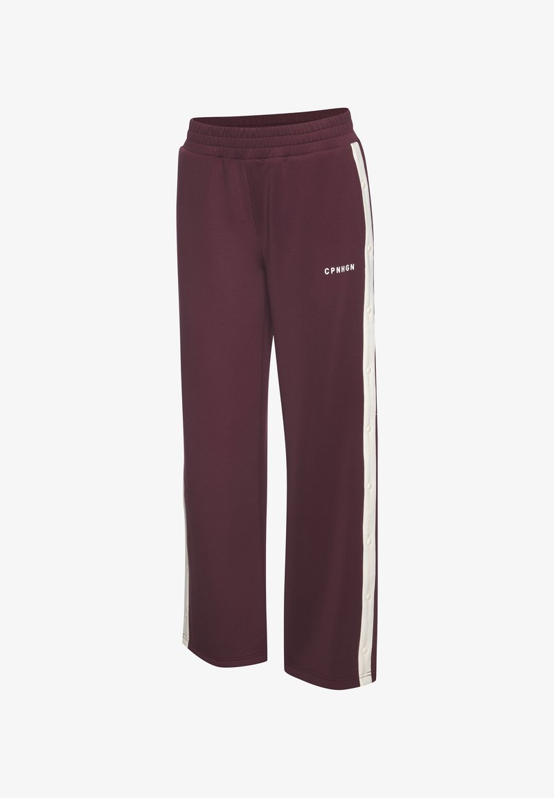 Vīna sarkanas sporta bikses ar platām kājām, elastīgu jostu, sānos baltām pogām un uzrakstu "CPNHGN" baltā krāsā priekšpusē.