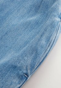Material de denim de un blue deschis, cu o textură netedă, având o țesătură diagonală subtilă și o margine cusută cu grijă.