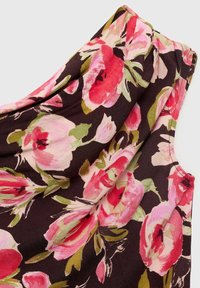 Tissu sombre avec un grand motif floral rose et rouge et des feuilles vertes, montrant un détail froncé près de la couture d'épaule d'un vêtement sans manches.