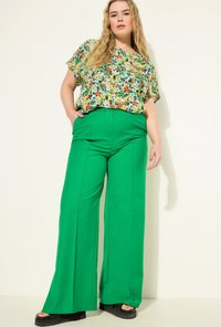 Bloes met korte mouwen in levendige kleuren; hoog-waisted groene wijde broek; zwarte platform sandalen. Geweven, casual ensemble.