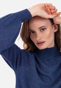 Pull bleu tricoté à col montant et manches ballon. Texture douce et coupe ajustée mettent en valeur la silhouette moderne du vêtement.