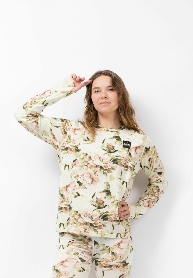 Langärmliges Blusenshirt in hellem Creme mit großen rosa und grünen Blumen. Mit einem Markenetikett auf der Brust und strukturiertem Stoff.