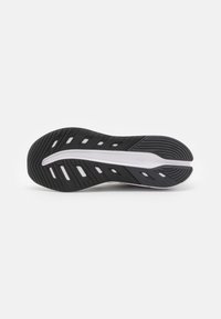 Semelle de chaussure de sport noire présentant un motif texturé avec des découpes circulaires, une semelle intermédiaire blanche et un design de lignes angulaires pour l'adhérence.