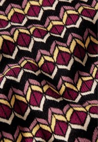 Tissu présentant un motif géométrique avec des formes bordeaux, roses et jaunes sur un fond noir, tissé avec une texture douce.