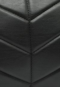 Materiale in pelle nera con superficie testurizzata, caratterizzato da un motivo a zigzag e dettagli di cucitura a contrasto. Finitura liscia e opaca.