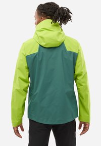 Veste imperméable présentant un design bicolore avec une partie supérieure verte vive et une partie inférieure verte plus foncée, en tissu texturé et avec une capuche ajustable.