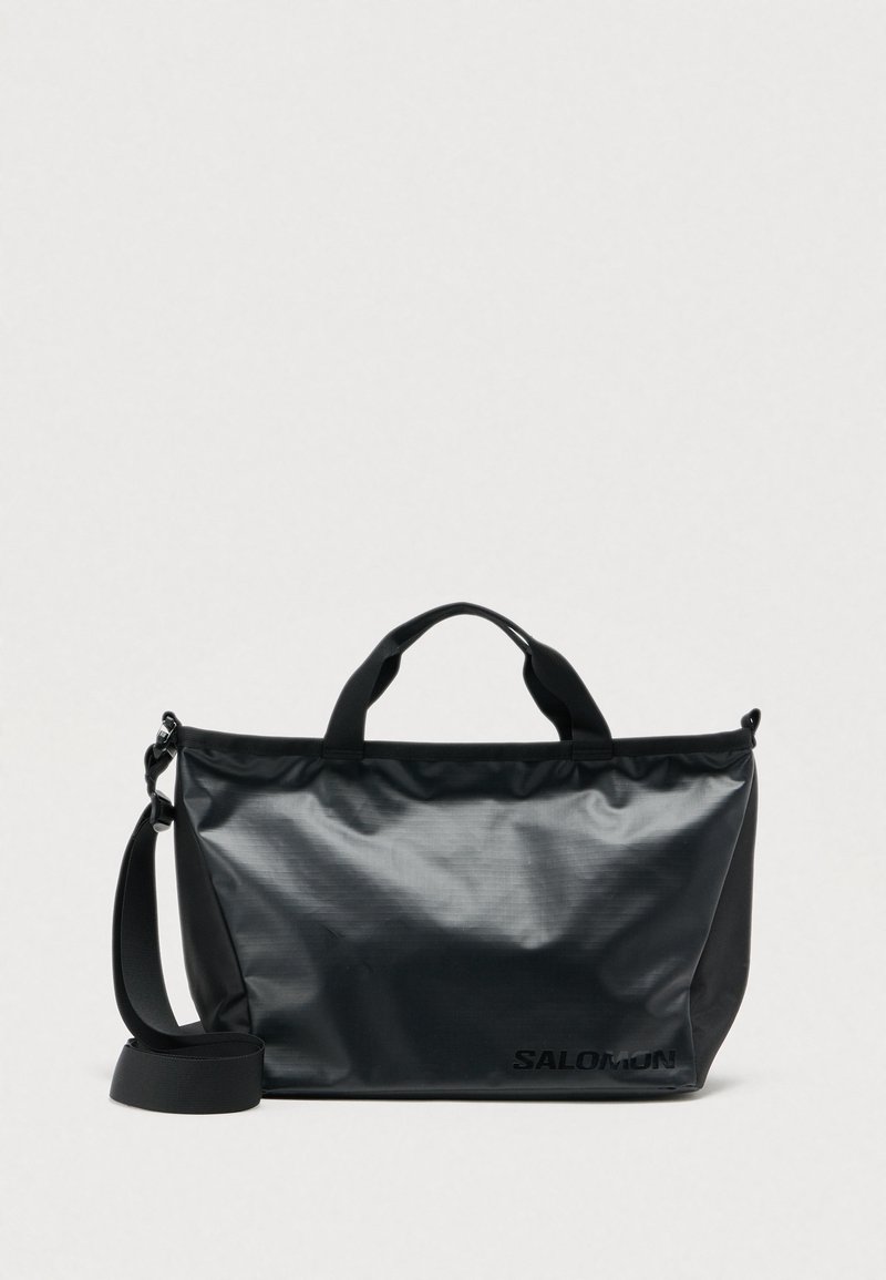 Μαύρη τσάντα με γυαλιστερό φινίρισμα, ορθογώνιο σχήμα, εξωτερικό λογότυπο, κοντά χερούλια και αφαιρούμενο ιμάντα ώμου για πολλαπλούς τρόπους μεταφοράς.