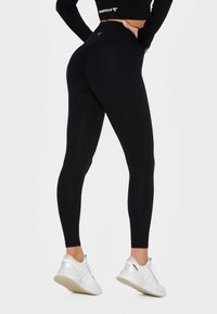 Black high-waisted leggings with a textured design, featuring ruching details at the back, paired with white sneakers.