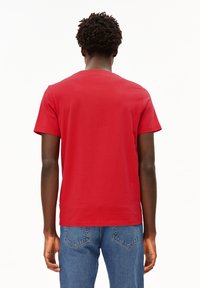 Rode katoenen T-shirt met ronde hals, korte mouwen en een eenvoudige uitstraling, gecombineerd met blauwe denim jeans. Achteraanzicht weergegeven.