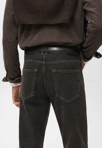 Jeans de denim negro con corte recto, dos bolsillos traseros y un cinturón con acabado suave. La tela tiene una ligera textura.