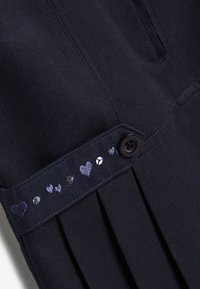 Marineblaue Faltenrock mit einem Knopfverschluss, der einen Bund mit herzförmiger Stickerei und dekorativen Strasssteinen verziert.