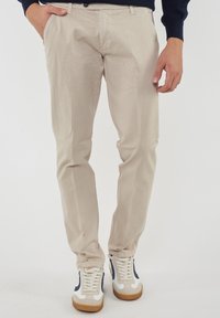 Pantaloni in cotone beige con una vestibilità slim, dotati di zip e tasche. Abbinati a sneaker bianche con dettagli blu navy e suola in gomma.
