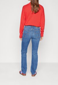 Modré džíny z denimu s rovnými nohavicemi, vyznačující se dvěma zadními kapsami a středním pasem, doplněné o pruhovaný červený svetr.