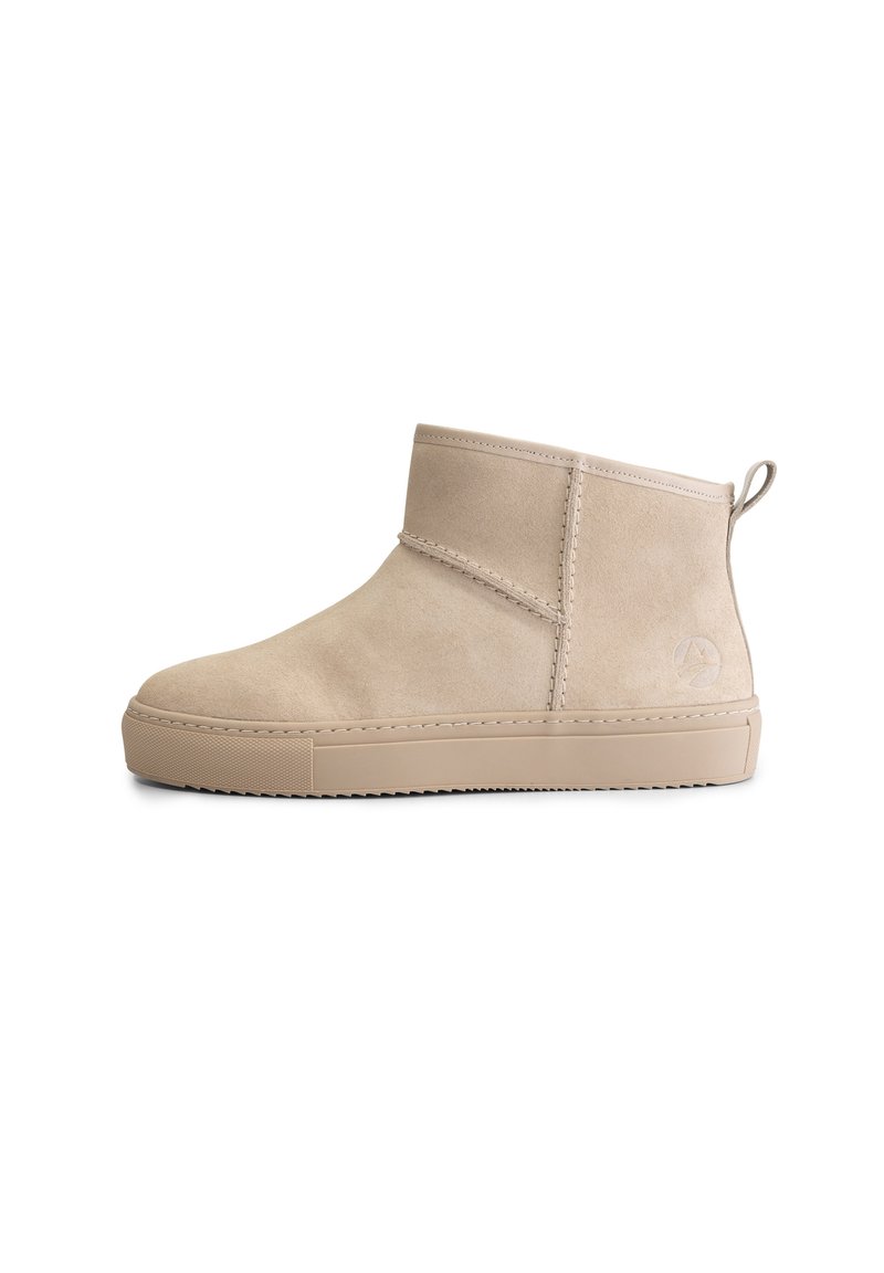 Beige suède enkellaars met platte rubberen zool, zijnaaddetails, een aantrekbandje bij de hak en een subtiele geëtste logo nabij de achterkant.