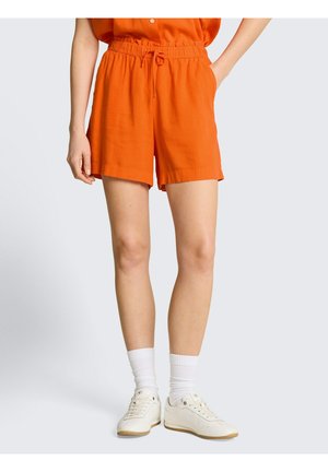 Persoon draagt fel oranje short met trekkoord, gecombineerd met witte crew-sokken en witte sneakers, tegen een effen lichte achtergrond.