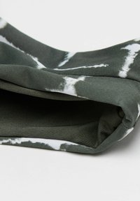 Tmavě zelená látka s bílým tie-dye vzorem, měkká textura, pečlivě složená, odhalující hladkou vnitřní podšívku.