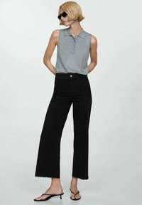 Gray sleeveless polo with three buttons, paired with high-waisted black wide-leg jeans featuring raw hems and black strappy sandals.