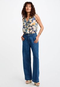 Ermeløs bluse med volang i yellow og blå mønstre, kombinert med høyt liv, vide blå denimjeans og espadrille sandaler.