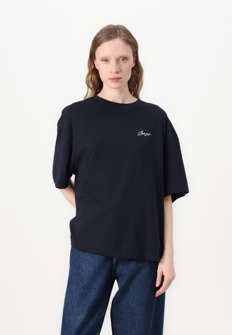 T-shirt en coton bleu marine avec un col rond et des manches courtes amorties. Présente un logo brodé blanc discret sur la poitrine.