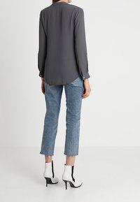 Blusa gris de manga larga con dobladillo redondeado, combinada con vaqueros cropped azul claro y botines de tacón en blanco y negro.