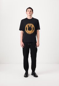 Sort bomuld T-shirt med et cirkulært orange grafisk design, parret med sorte sweatpants og sorte sko. Enkel, afslappet pasform.