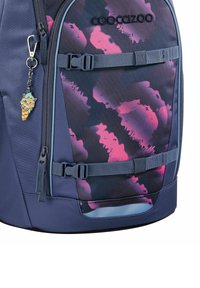 Sac à dos avec une base bleu foncé, présentant un motif abstrait multicolore en rose. Comprend un zip avec un porte-clés en forme de personnage.