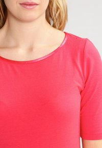 Tætsiddende, kortærmet top i lys pink bomuld med en rundet halsudskæring og en glansfuld trim. Glat tekstur uden mønstre eller detaljer.