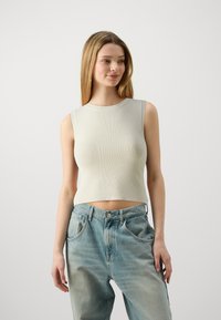 Šviesiai pilkas, storas, be rankovių crop top'as su apvaliu iškirpimu, derinamas su plačiomis, išblukusiomis mėlynomis džinsomis ir sagstomu juosmeniu.