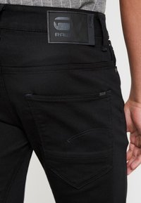 Svarta denimjeans med en slät textur, en G-Star RAW läderpatch på baksidan och diskret sömnad på fickorna.