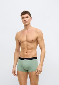 Zielone bokserki z czarnym paskiem w talii z napisem "BOSS", wykonane z miękkiego materiału, o dopasowanym, nowoczesnym kroju.