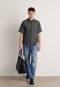 Μ αύρη και άσπρη καρό μπλούζα με κοντό μανίκι, συνδυασμένη με ανοιχτό μπλε τζιν ίσιας γραμμής. Το μοντέλο κρατά μια μαύρη δερμάτινη τσάντα.