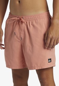 Roze kupaće hlače napravljene od lagane tkanine. Imaju elastičnu traku u struku, vezicu i oznaku loga na donjem rubu.