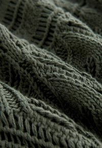 Tissu tricoté vert avec un motif texturé, mettant en avant des points en relief et une apparence douce et épaisse. Le tissage complexe ajoute de la profondeur.