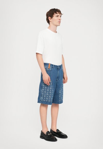 Denim shorts with patterned embroidery on side panels, blue color, loose fit, paired with a plain white t-shirt and black loafers.