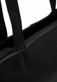 Zwarte leren tote bag met twee stevige handvatten, ritssluiting en zichtbare stiksels. Bevat een geperst logo aan de zijkant.