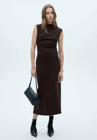 Rochie maro ajustată cu gât înalt și design fără mâneci, asociată cu o geantă neagră și tocuri negre lucioase. Țesătură texturată pe un fundal neutru.