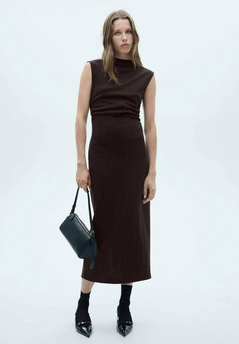 Rochie maro ajustată cu gât înalt și design fără mâneci, asociată cu o geantă neagră și tocuri negre lucioase. Țesătură texturată pe un fundal neutru.
