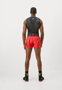 Black sleeveless top with textured design, paired with red shorts featuring black zigzag accents and an elastic waistband. Black footwear with yellow details.